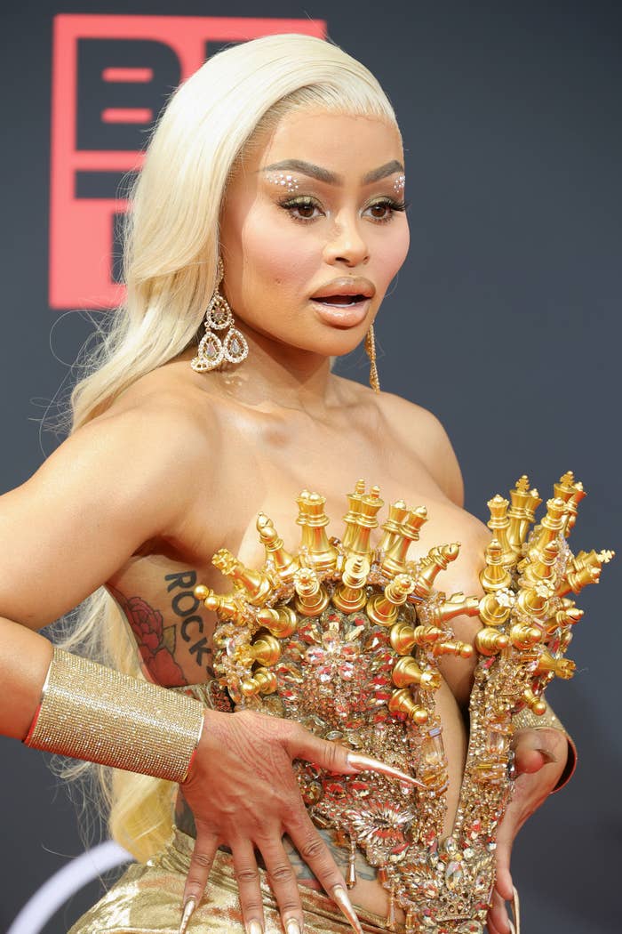 A closeup of Blac Chyna on the red carpet wearing a top encrusted with gold chess pieces