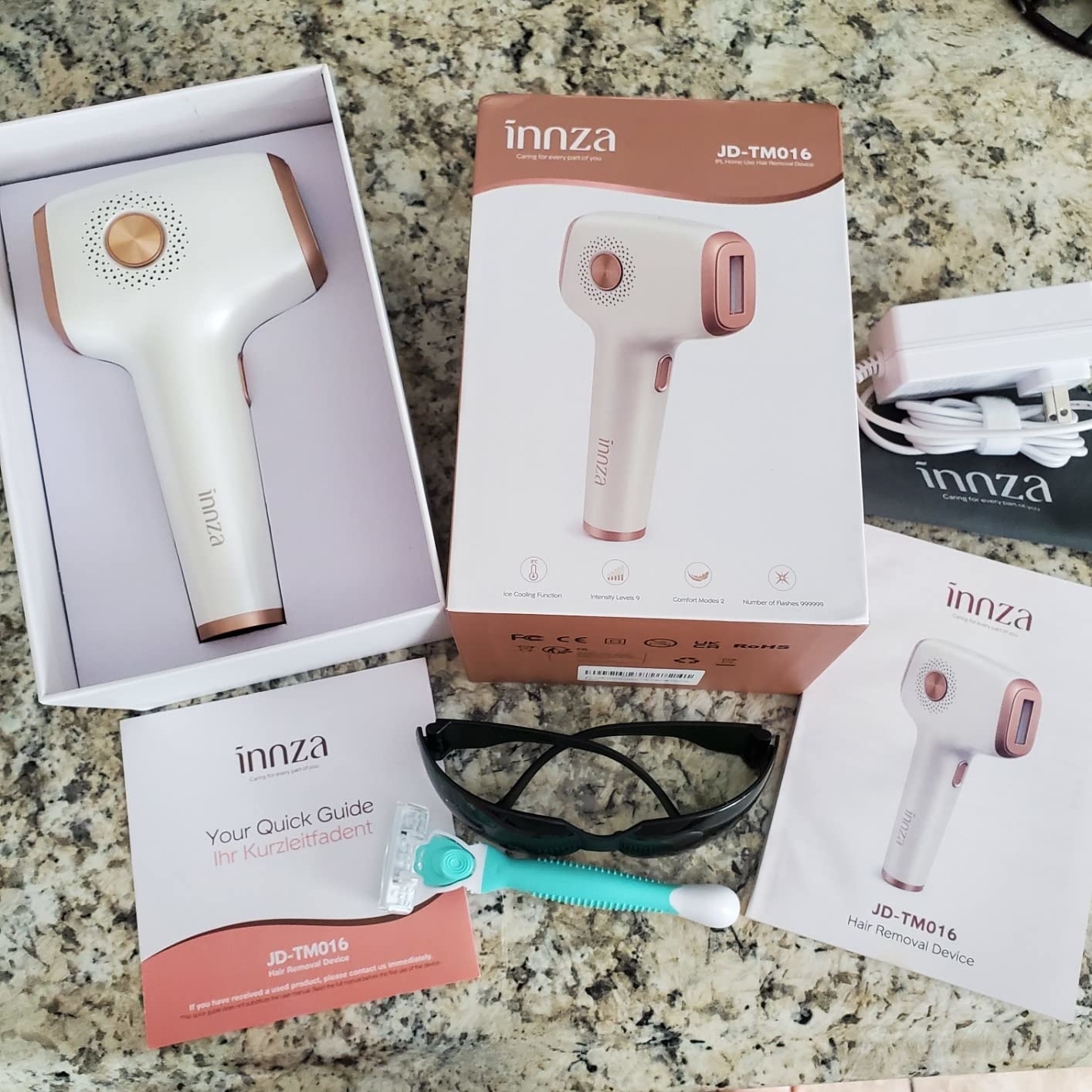 a reviewer photo of the laser hair removal tool in the box with a pair of sunglasses, a razor, instructional manual, and charging cable