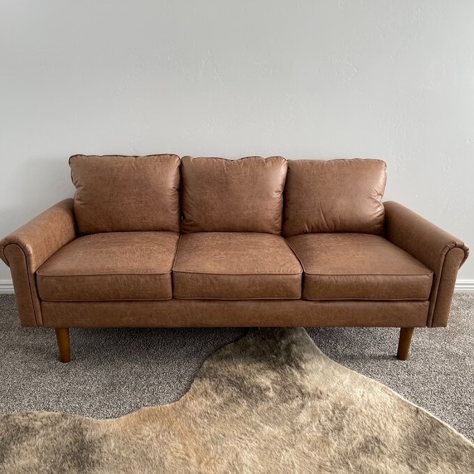 Reviewer&#x27;s photo of brown pleather couch with rug.