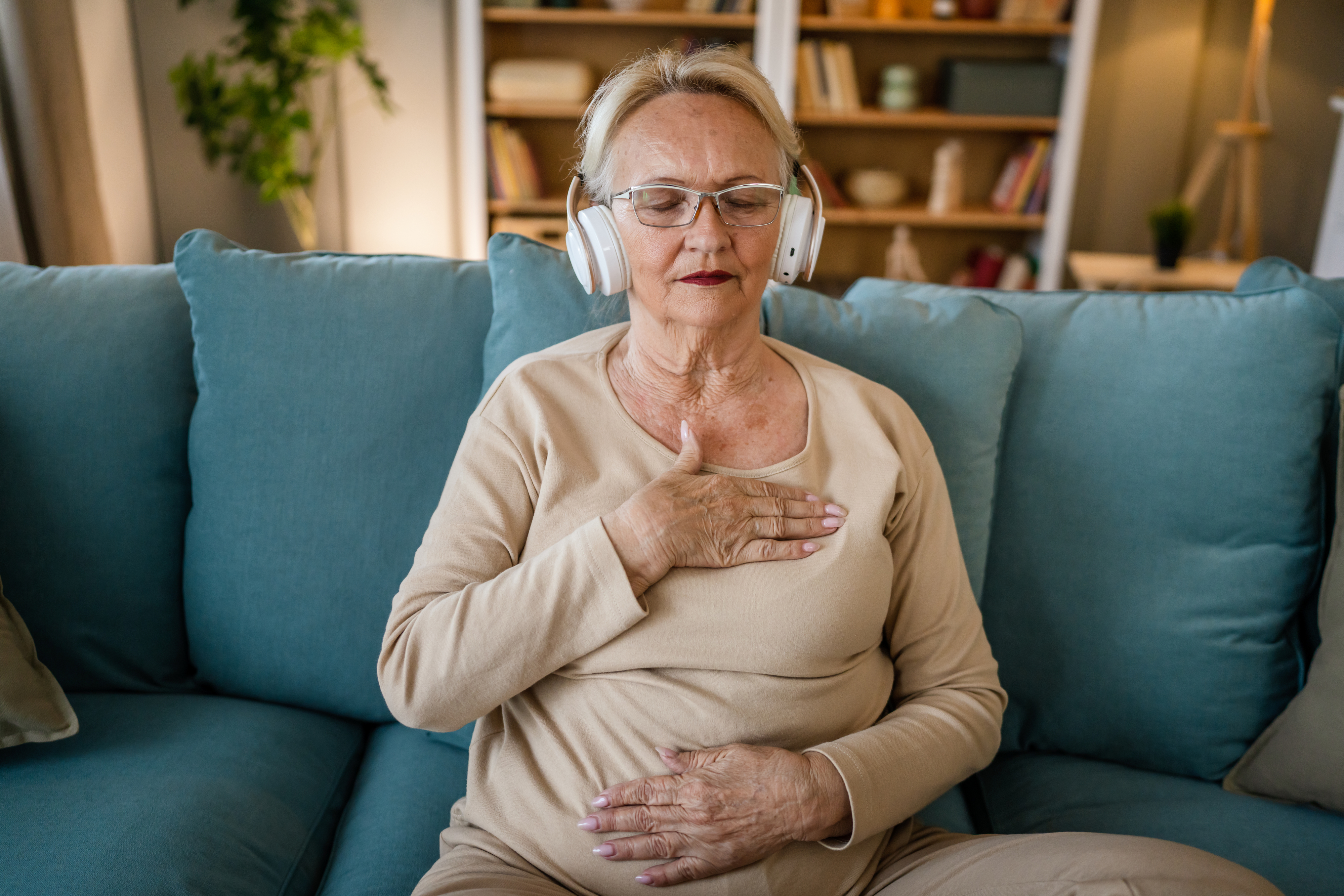 A woman with her hand on her chest listening to her headphones