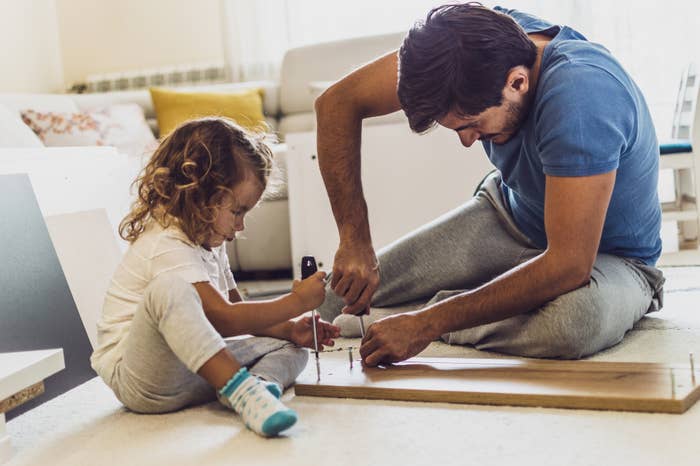 little girl using a screwdriver to help her dad put furniture together