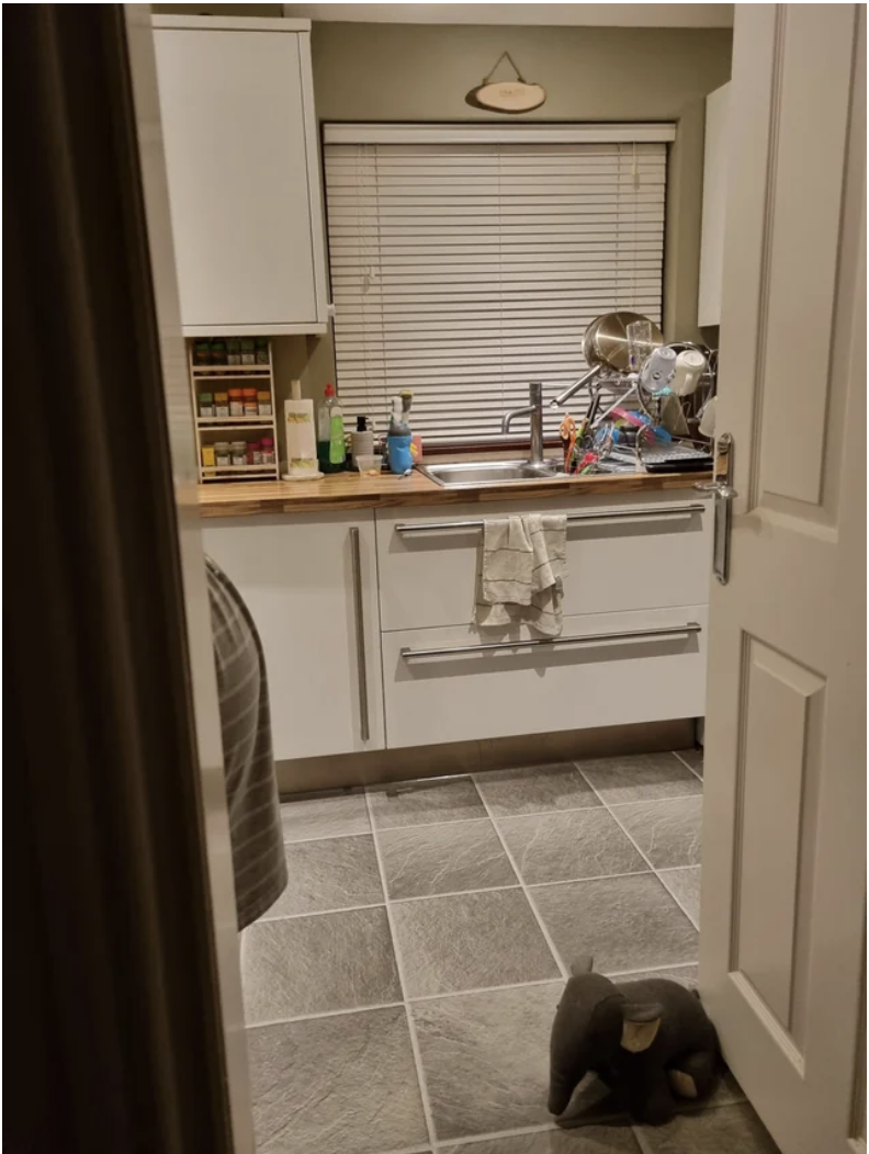 Woman hiding behind an open door in a kitchen, but her belly is visible just beyond it