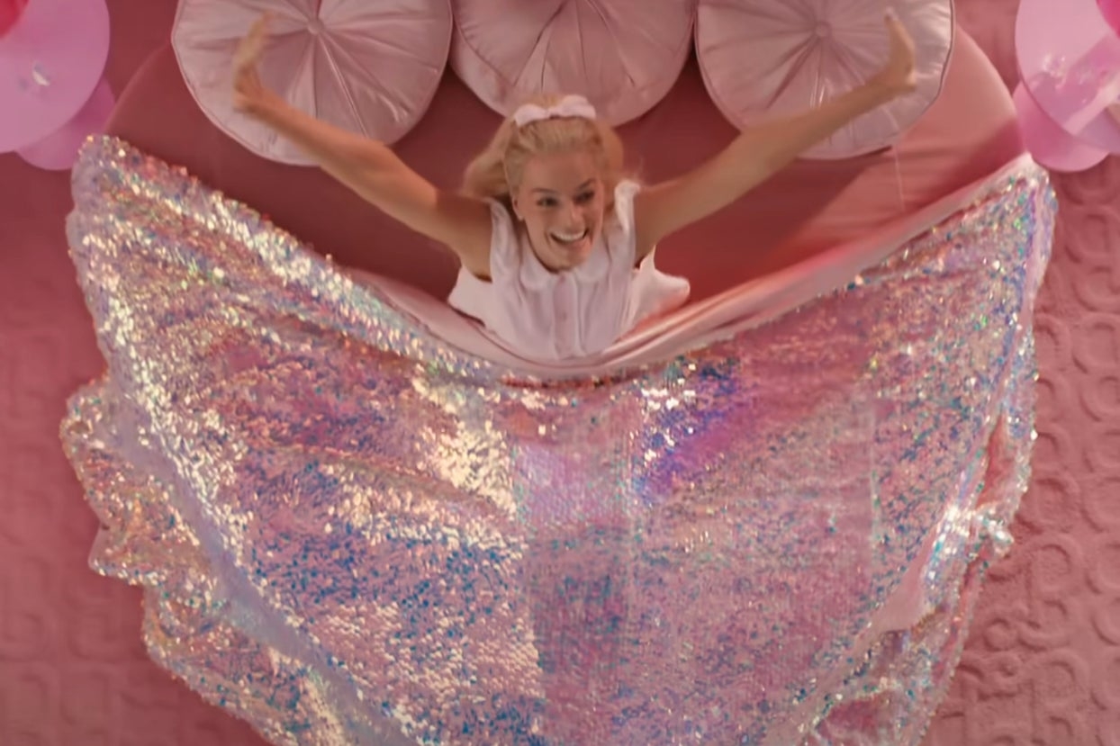Margot Robbie stretching and smiling as she wakes up in a sparkly bed as Barbie