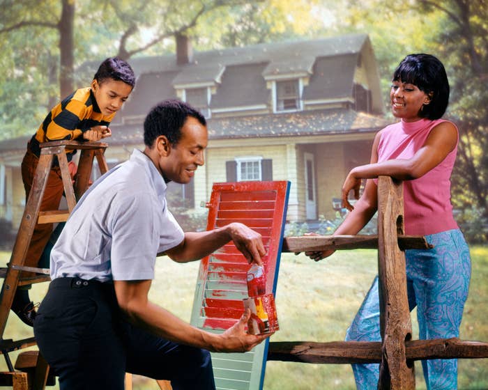A man painting a window shutter as his wife and child look on