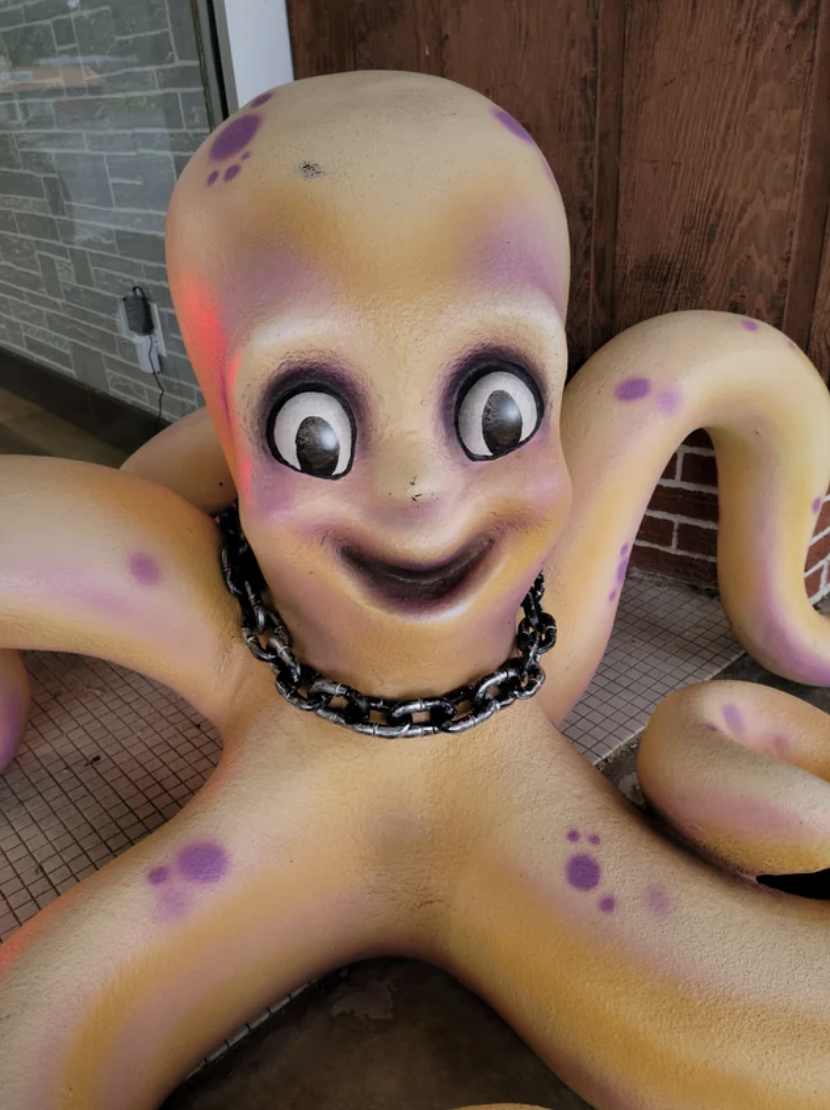 A huge octopus sculpture with a chain around its neck and a large, toothless smile and huge, staring eyes