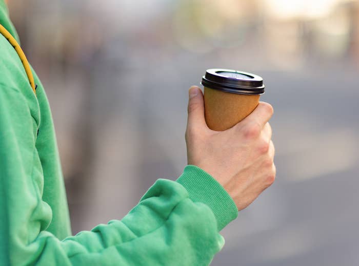 A person holds a paper cup of coffee