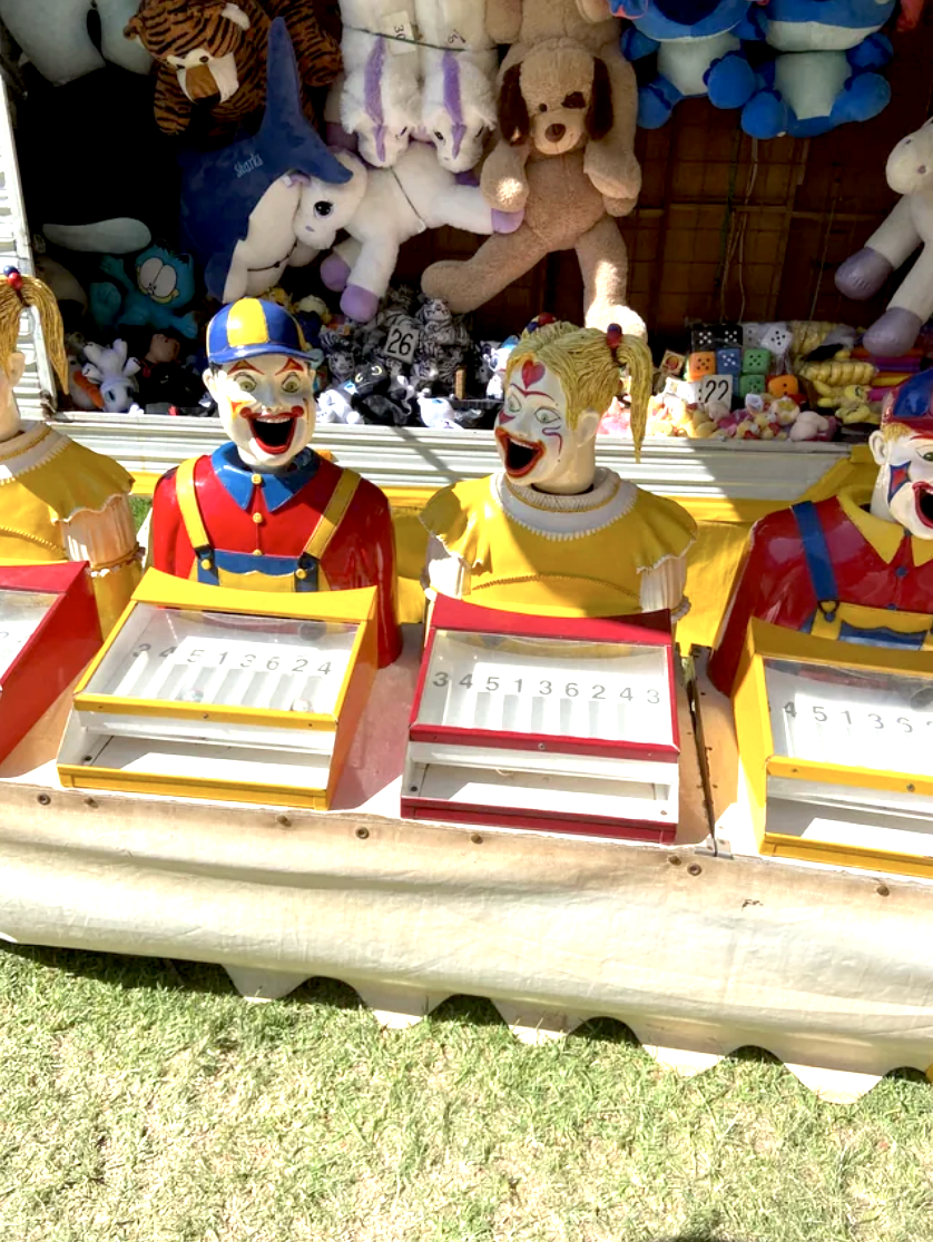 Laughing, scary, brightly painted clown figures with open mouths as smiles that are part of a fair game