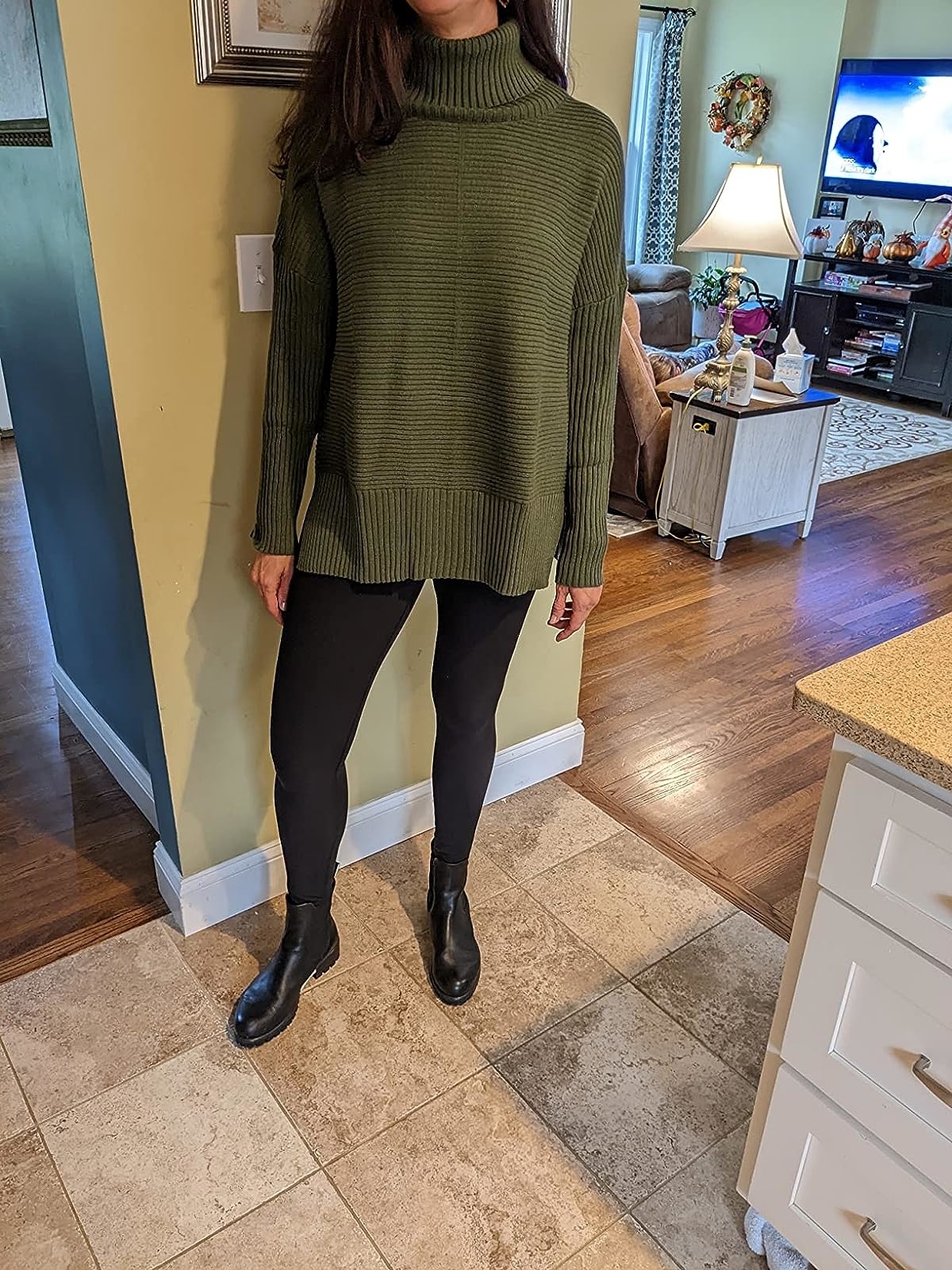 Reviewer wearing the green turtleneck with black leggings and ankle boots
