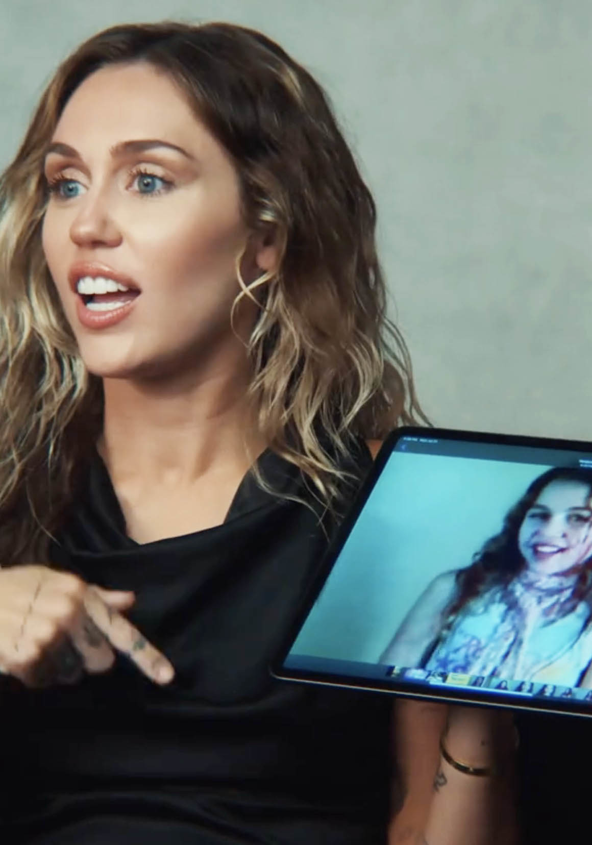 miley holding a tablet with a moment from her past on the screen