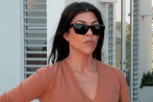 Kourtney Kardashian wears sunglasses, mouth pursed as if mad.