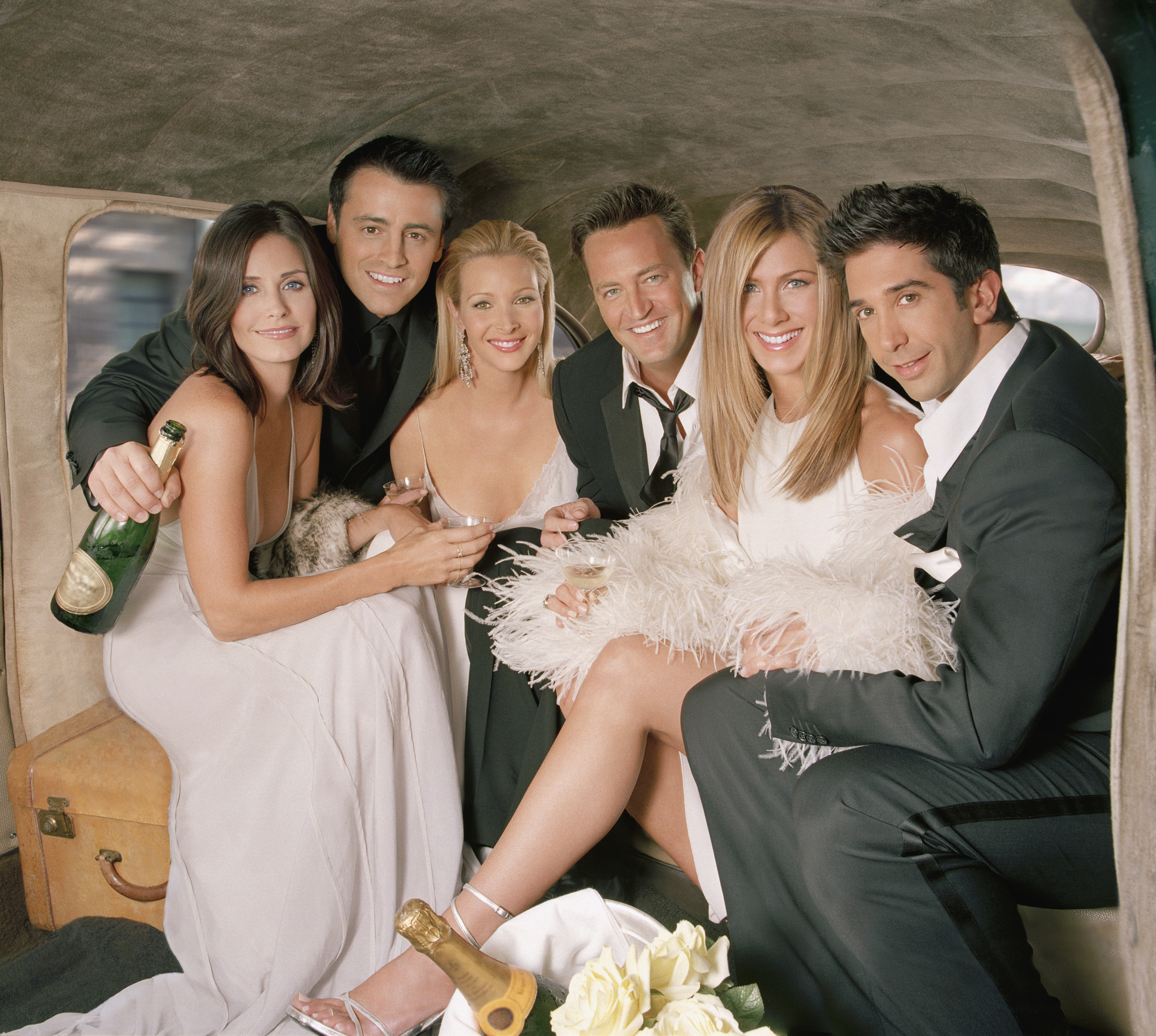 The six leads sitting together with bottles of champagne in a scene from the show