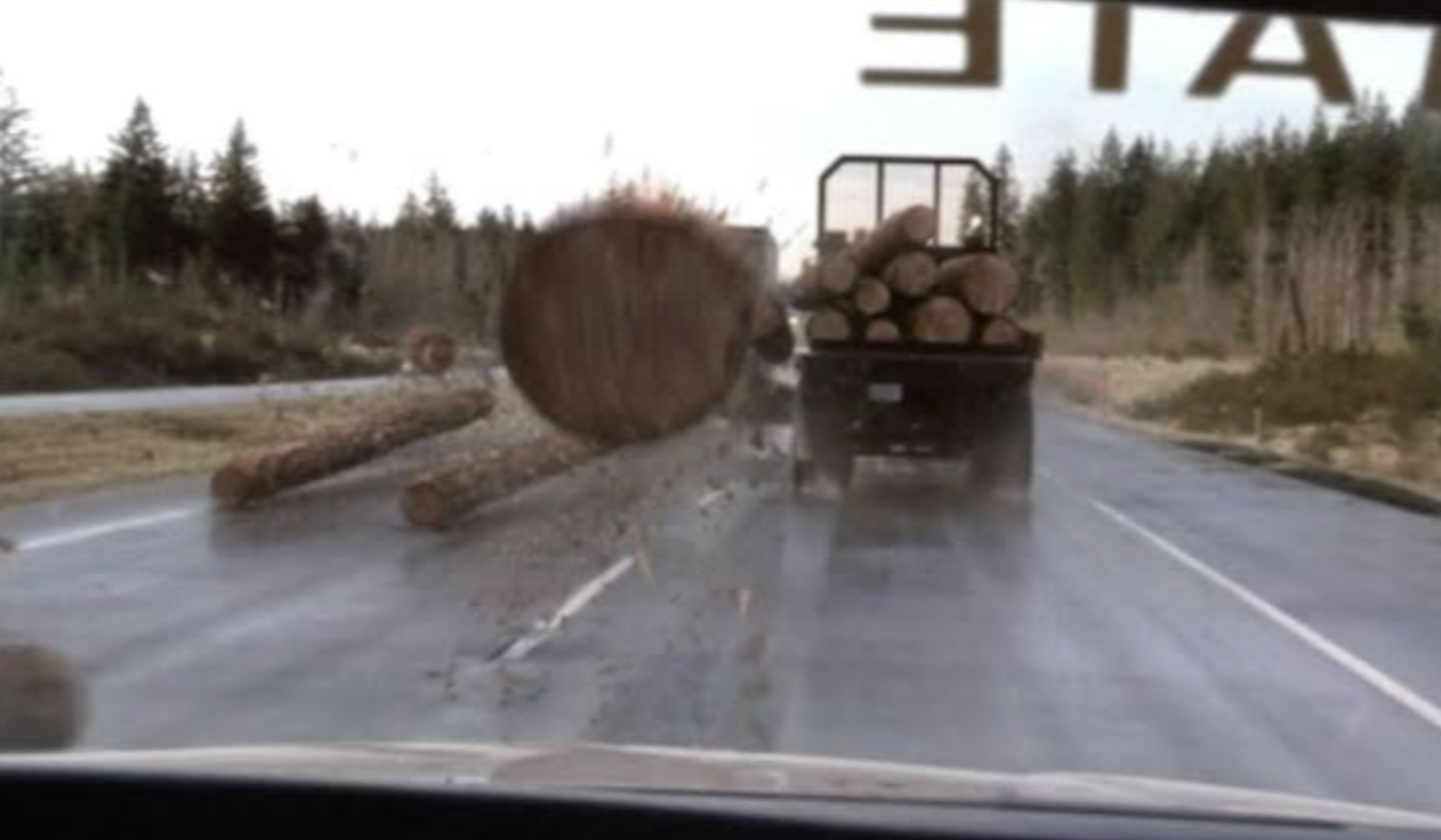 Logs flying out of a truck toward the car behind it