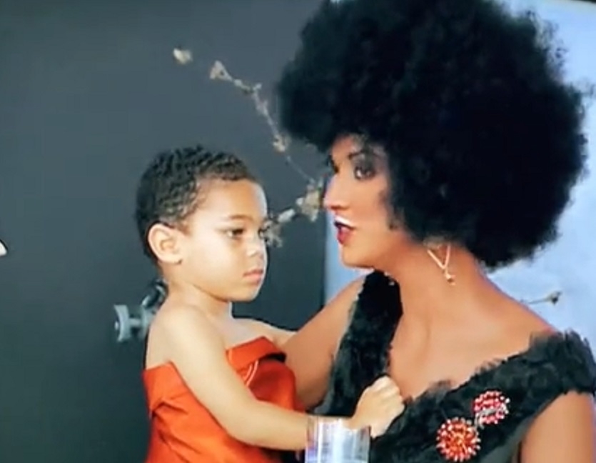 A white model in an afro holding a child