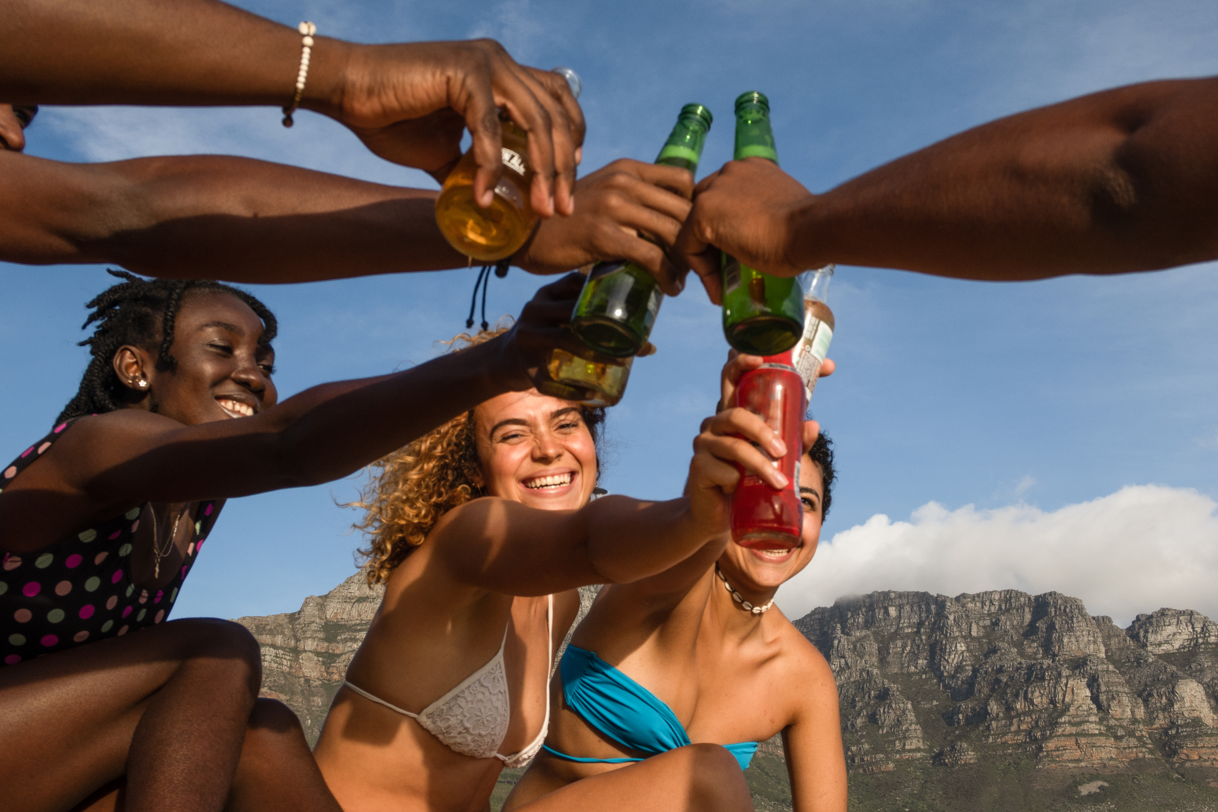 Young women in bathing suits clinking beer bottles together outdoors and smiling