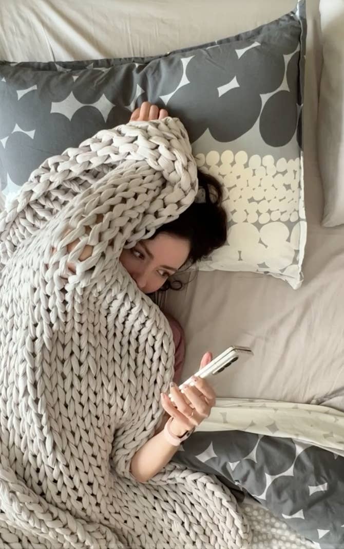 A person peeking at their phone from underneath their blanket