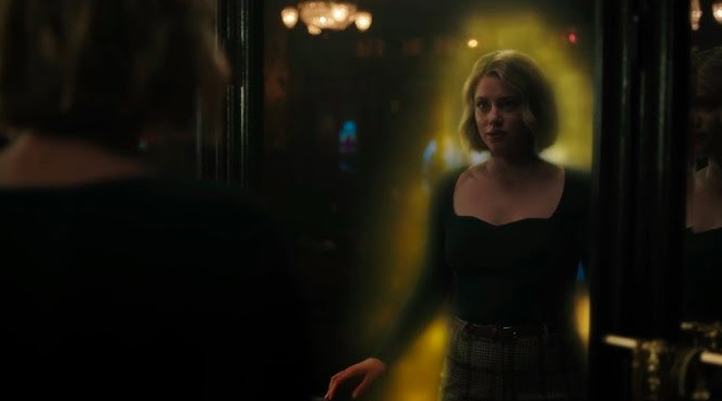 Betty, a young woman with a blonde bob, looks at herself in the mirror. She is surrounded by a glowing yellow aura.