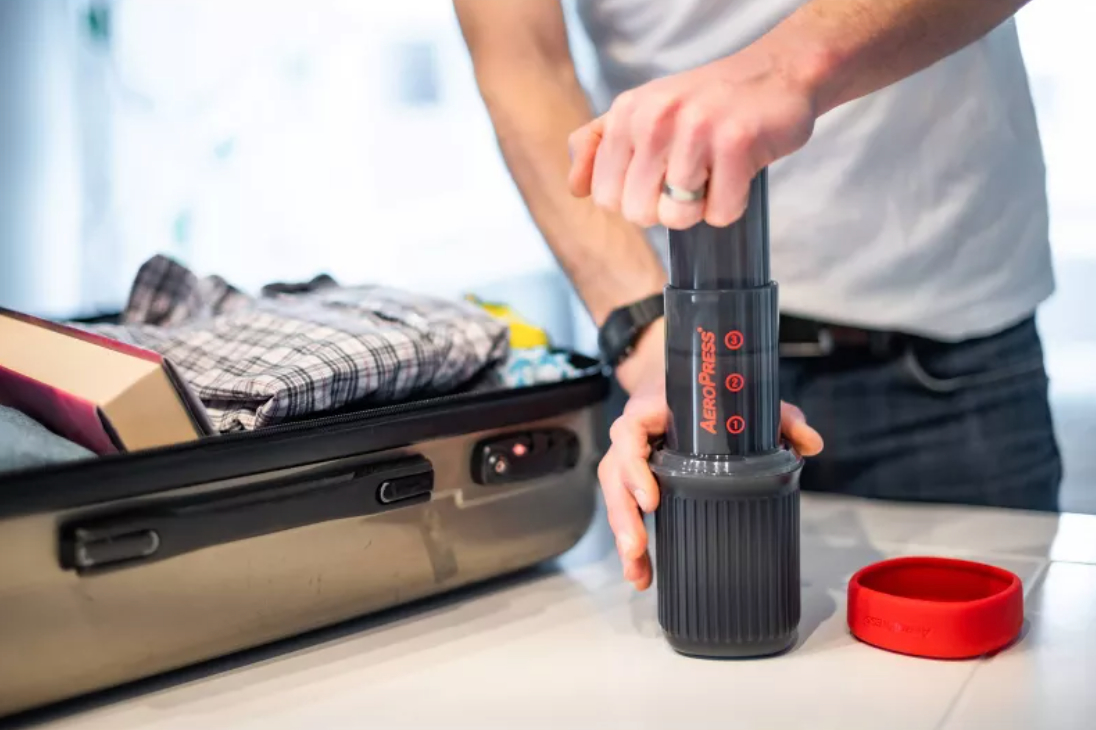 a person making coffee with an aeropress next to an open luggage