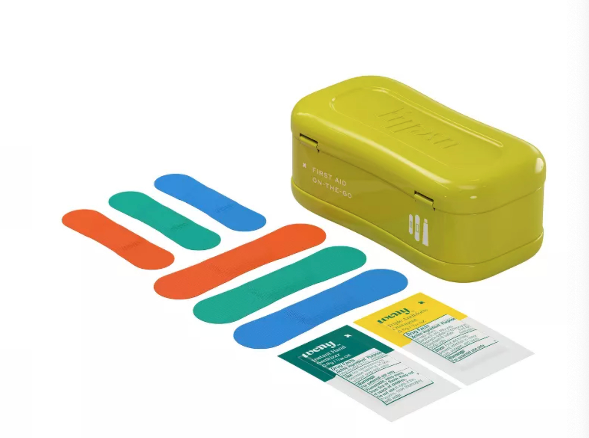 a green tin with colorful bandages and two medicine packets laid out next to it