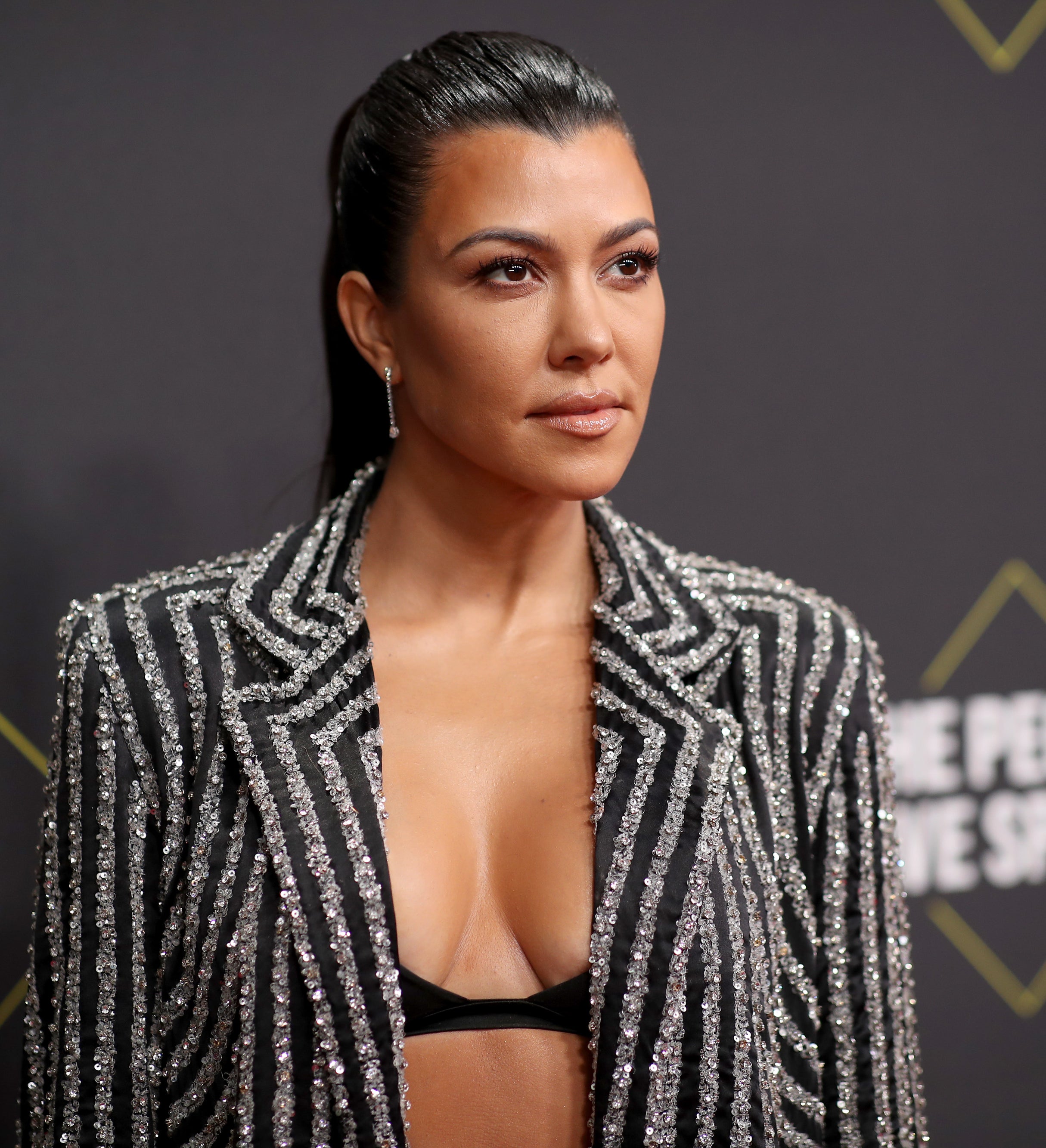 Closeup of Kourtney Kardashian in a bralette and a sequined striped jacket