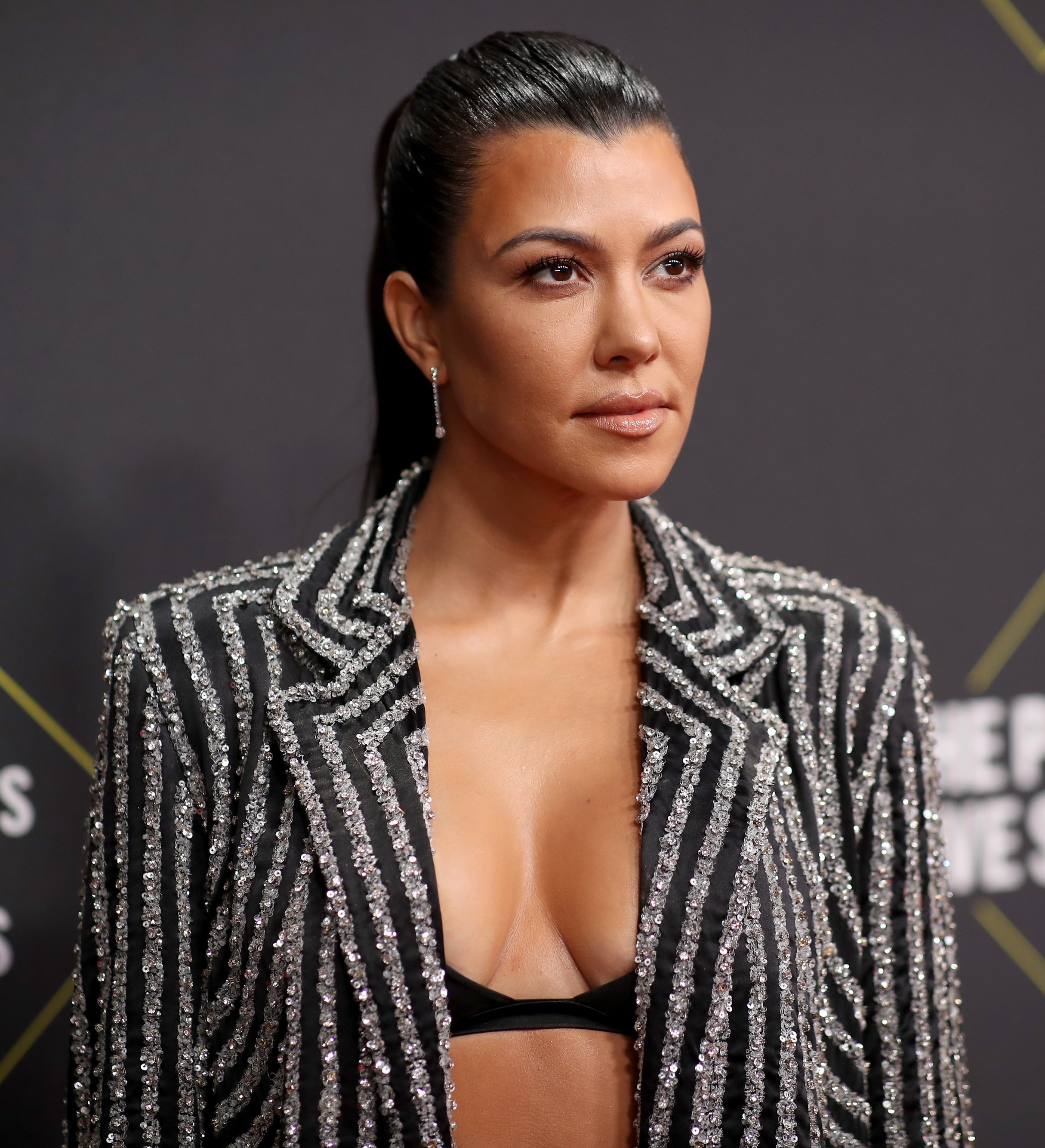 Closeup of Kourtney Kardashian in a bralette and a sequined striped jacket
