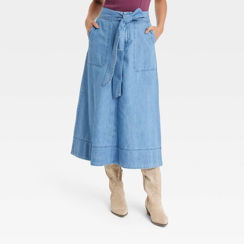 A model wearing a blue denim skirt with a red top and brown boots