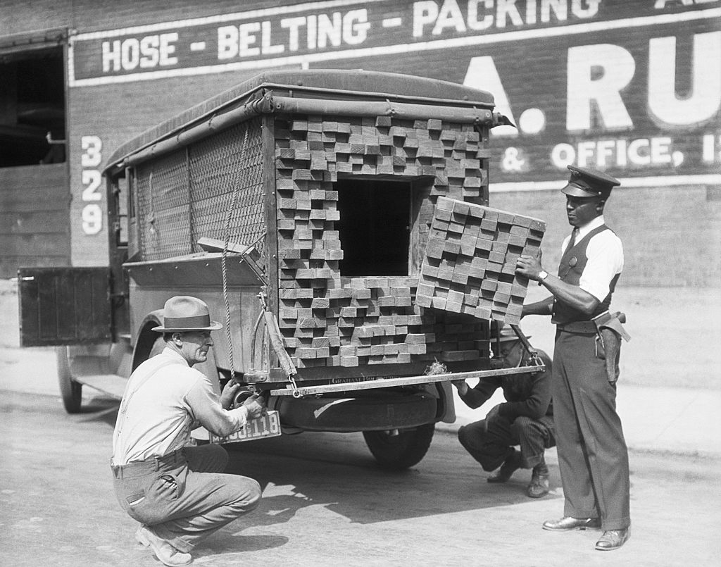 Two men next to a truck with blocks of &quot;wood&quot; and a small square hole in the back with a cutout piece of fake wood blocks
