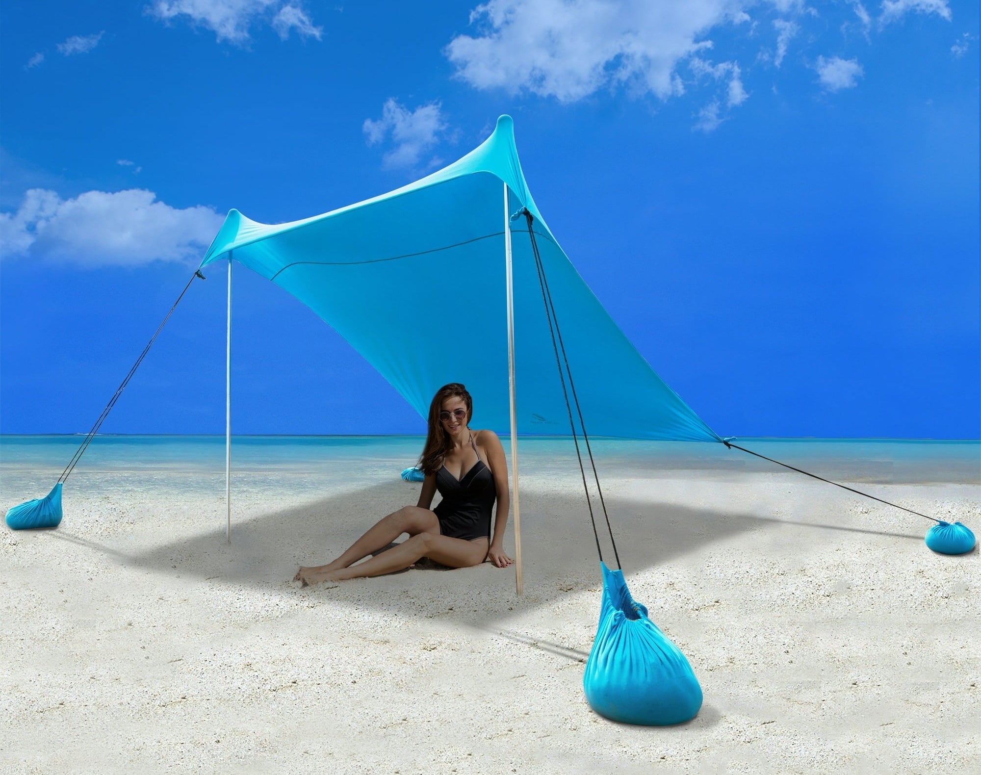 Person in swimwear sitting under a beach canopy tent on sand, with a blue sky background