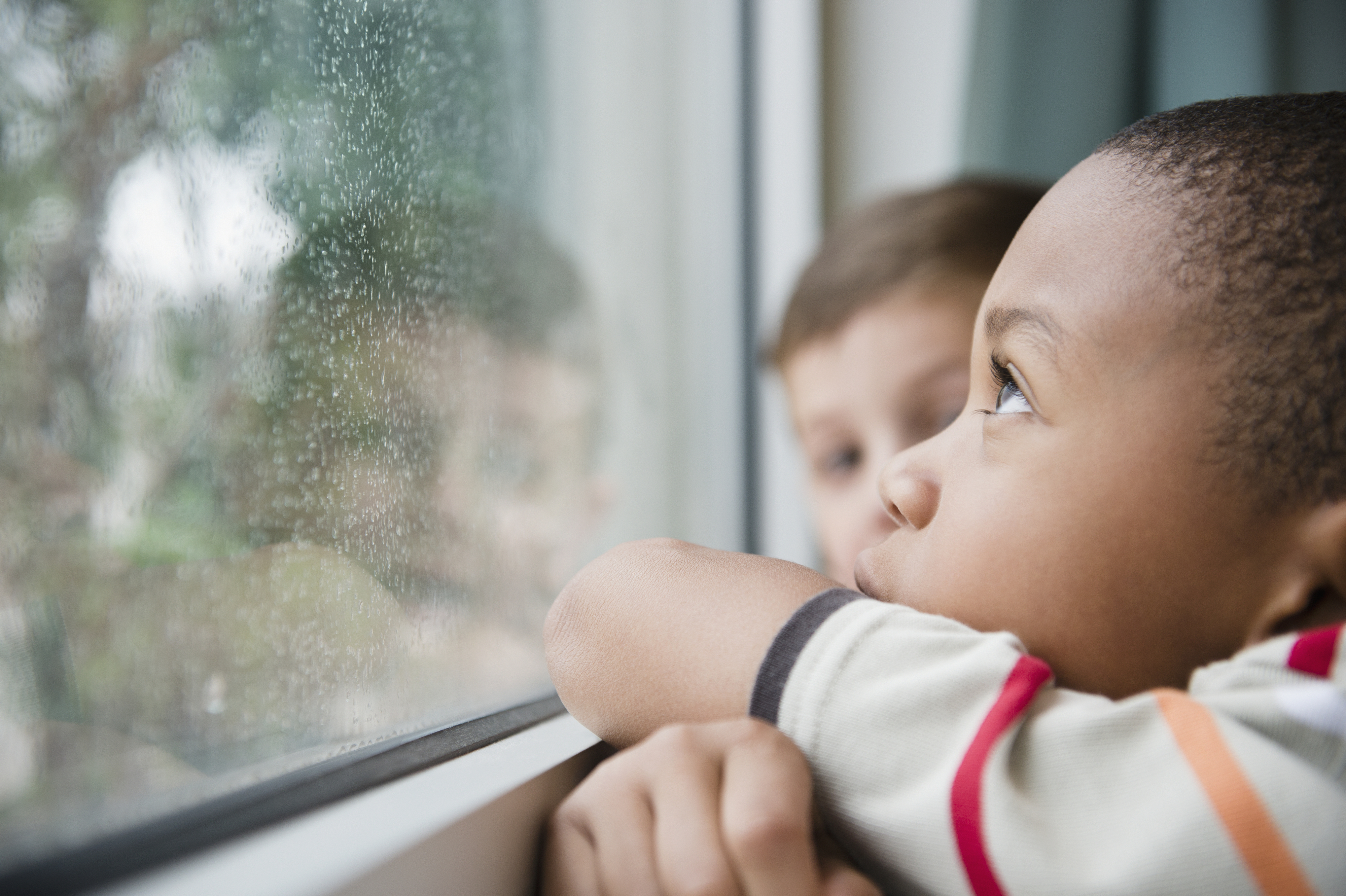 Two kids looking out the window on a rainy day