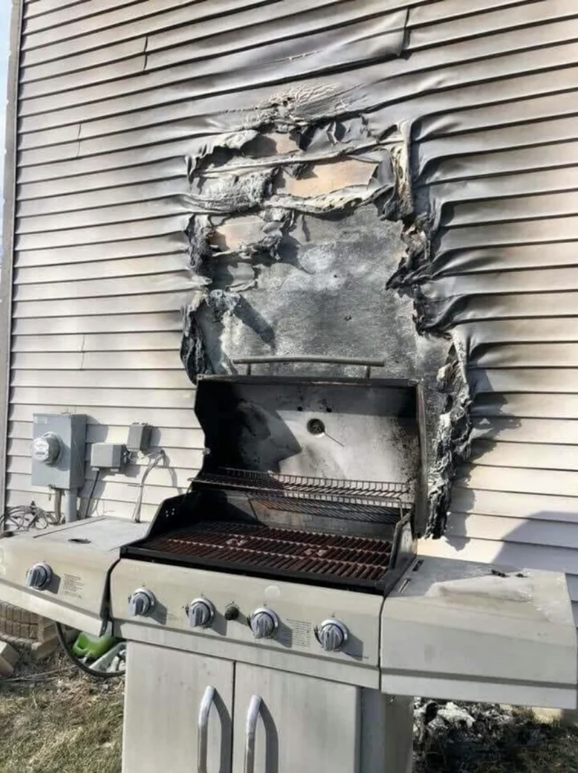A grill right up against a house that has the side paneling burned out