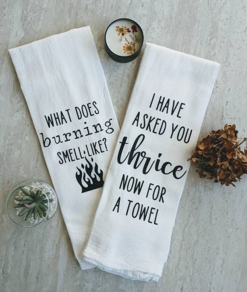 a white tea towel that says &quot;what does burning smell like?&quot; with a small flames icon and one that reads &quot;I have asked you thrice now for a towel&quot;