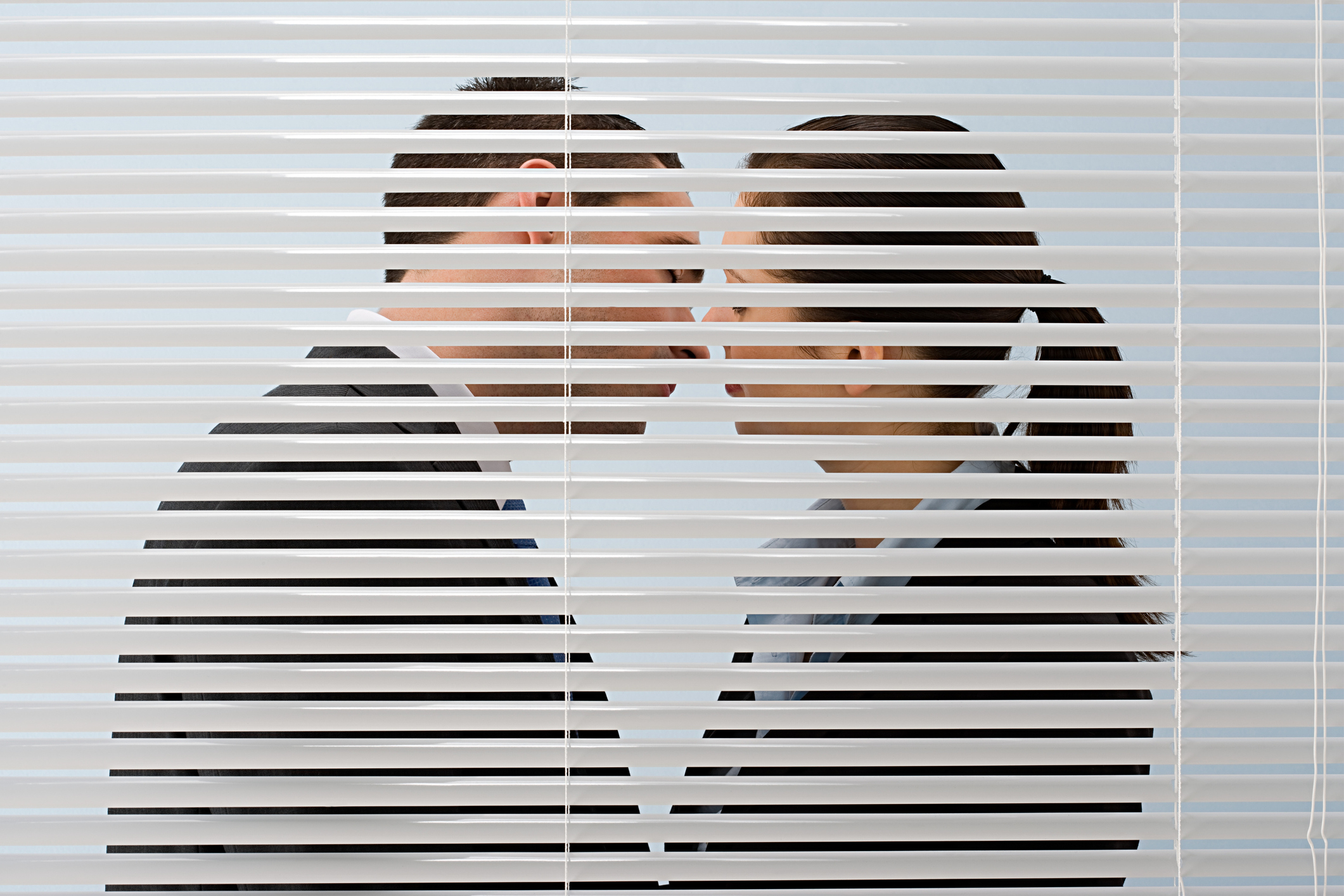 Coworkers about to kiss behind some blinds