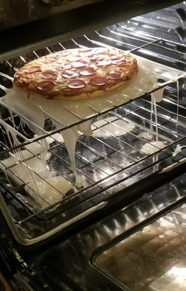 A pizza in the oven with a plastic cutting board under it that has completely melted in the oven