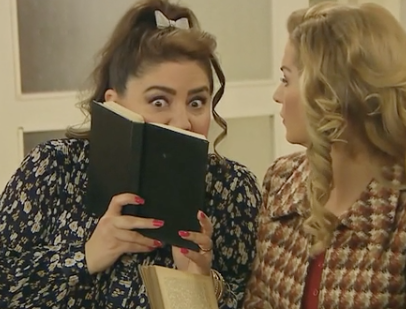 A woman holding a book over her mouth and leaning toward another woman