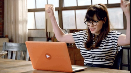 A woman sitting at a laptop and raising her hands triumphantly