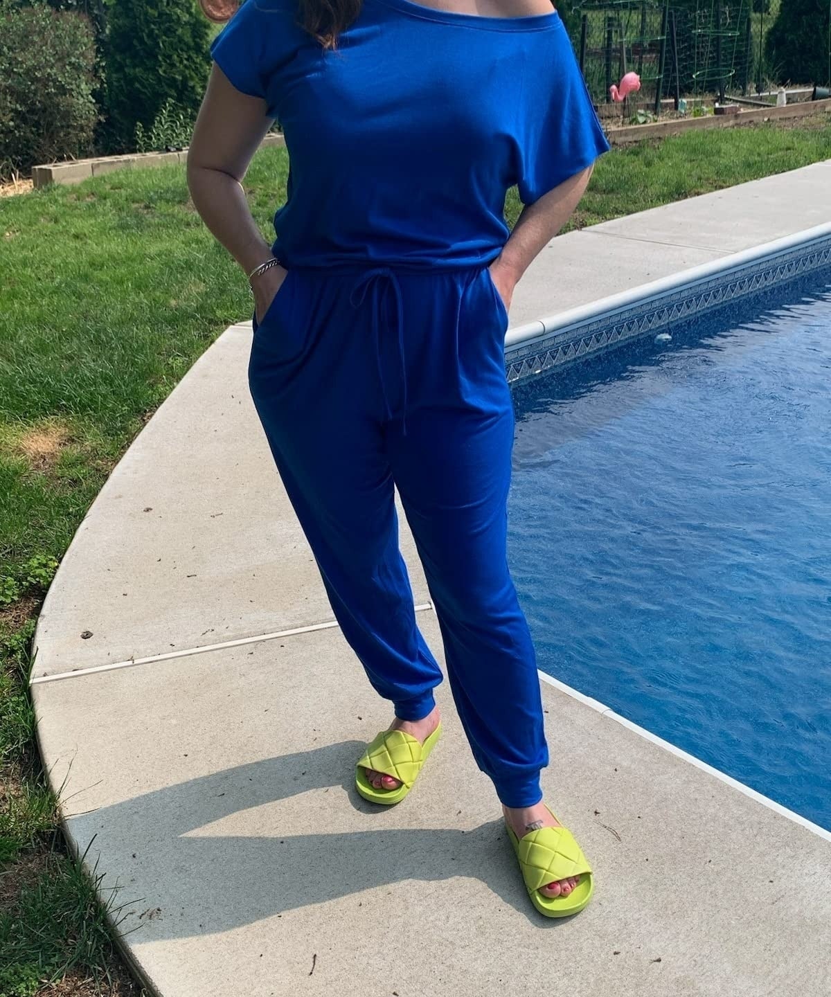 a reviewer wearing the blue jumpsuit and yellow sandals by a pool