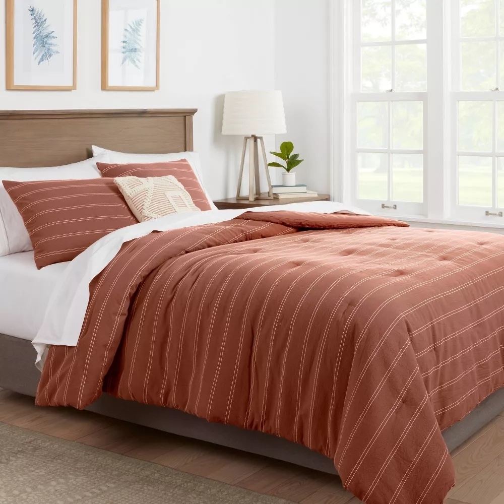 Striped burnt orange comforter and shams on a wooden bed with white sheets