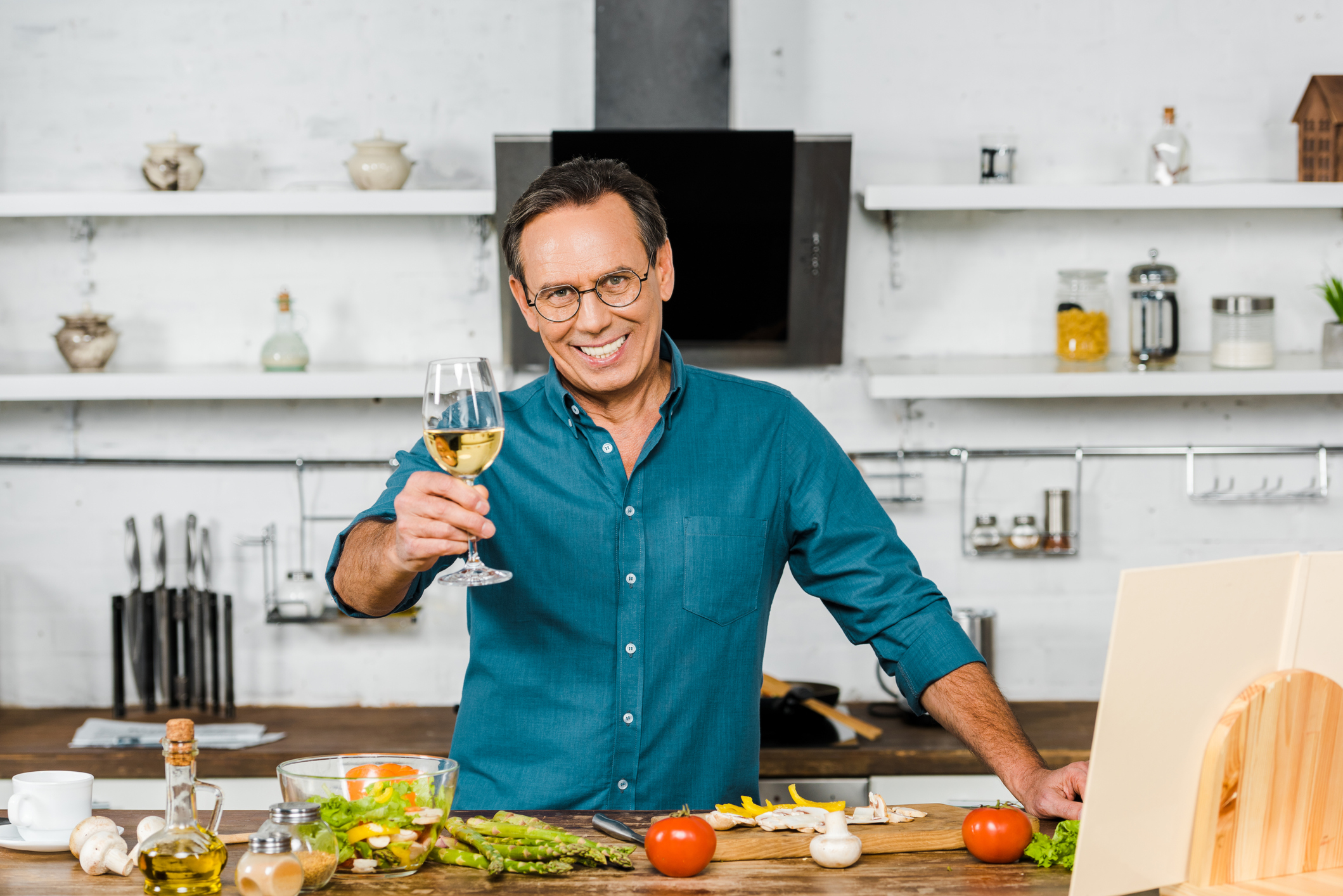 A man raising a glass and smiling as he cooks in the kitchen