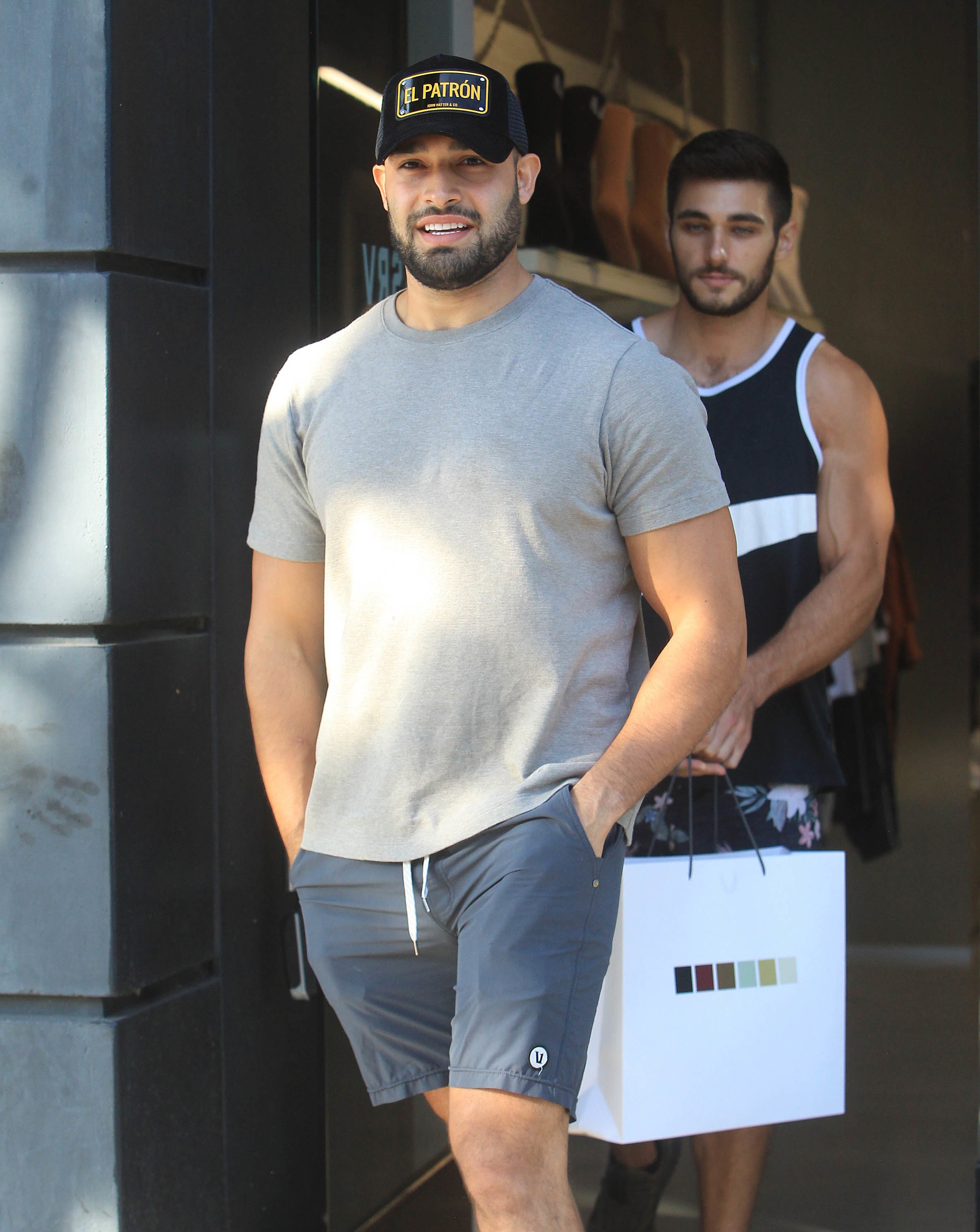 Close-up of Sam in shorts, T-shirt, and an El Patrón cap leaving a store