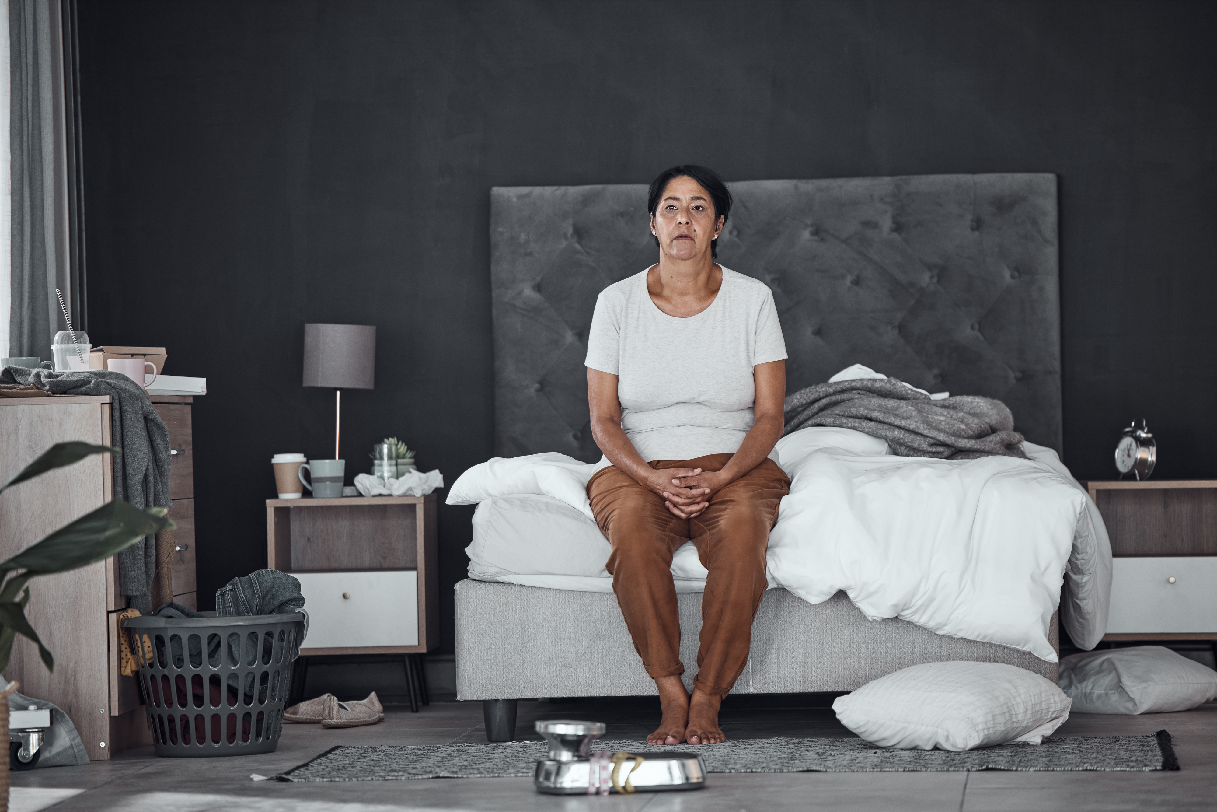 woman sitting at the edge of the bed with a mess around her