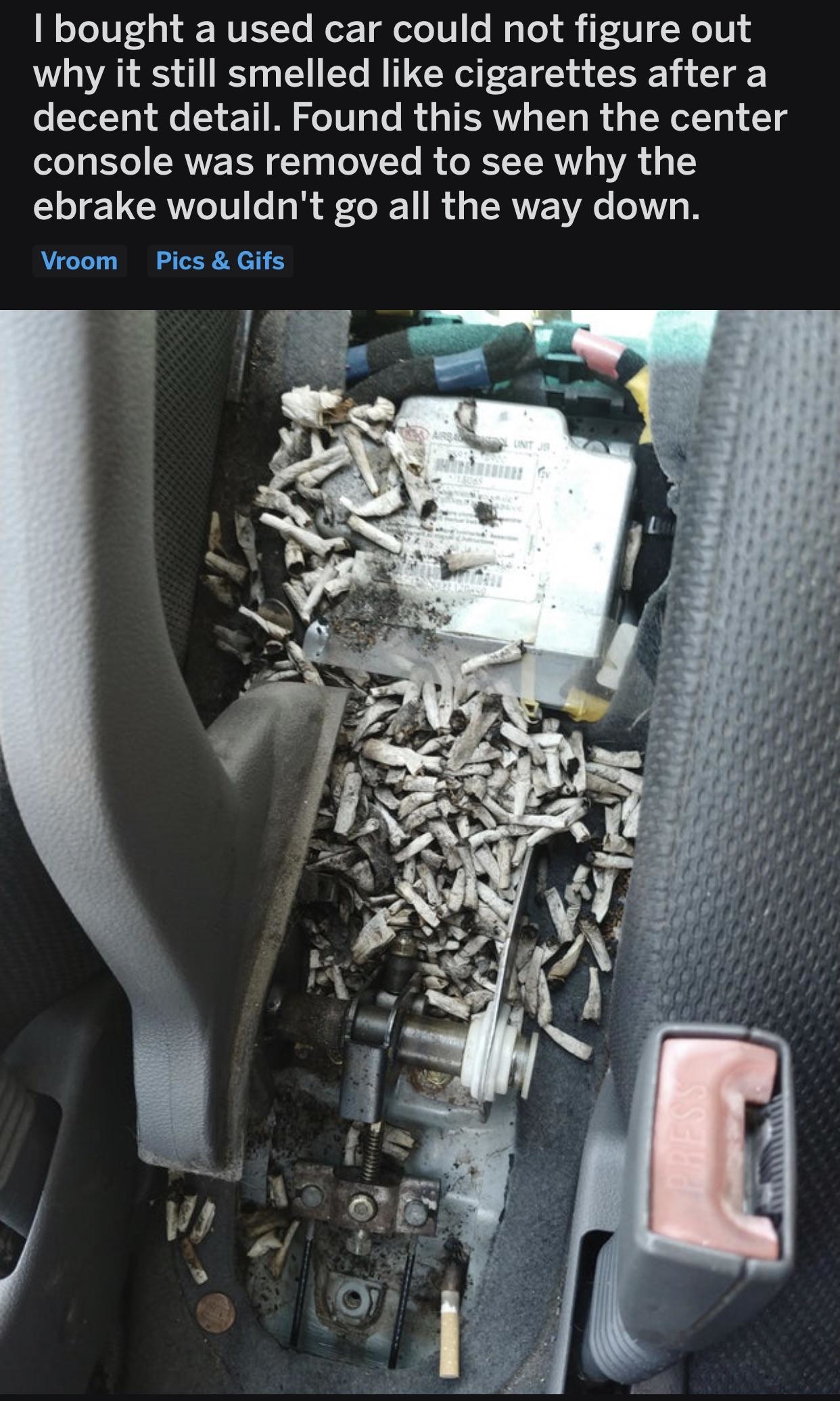 Person who just bought a used car finds a huge pile of cigarette butts behind the center console — which explains the cigarette smell