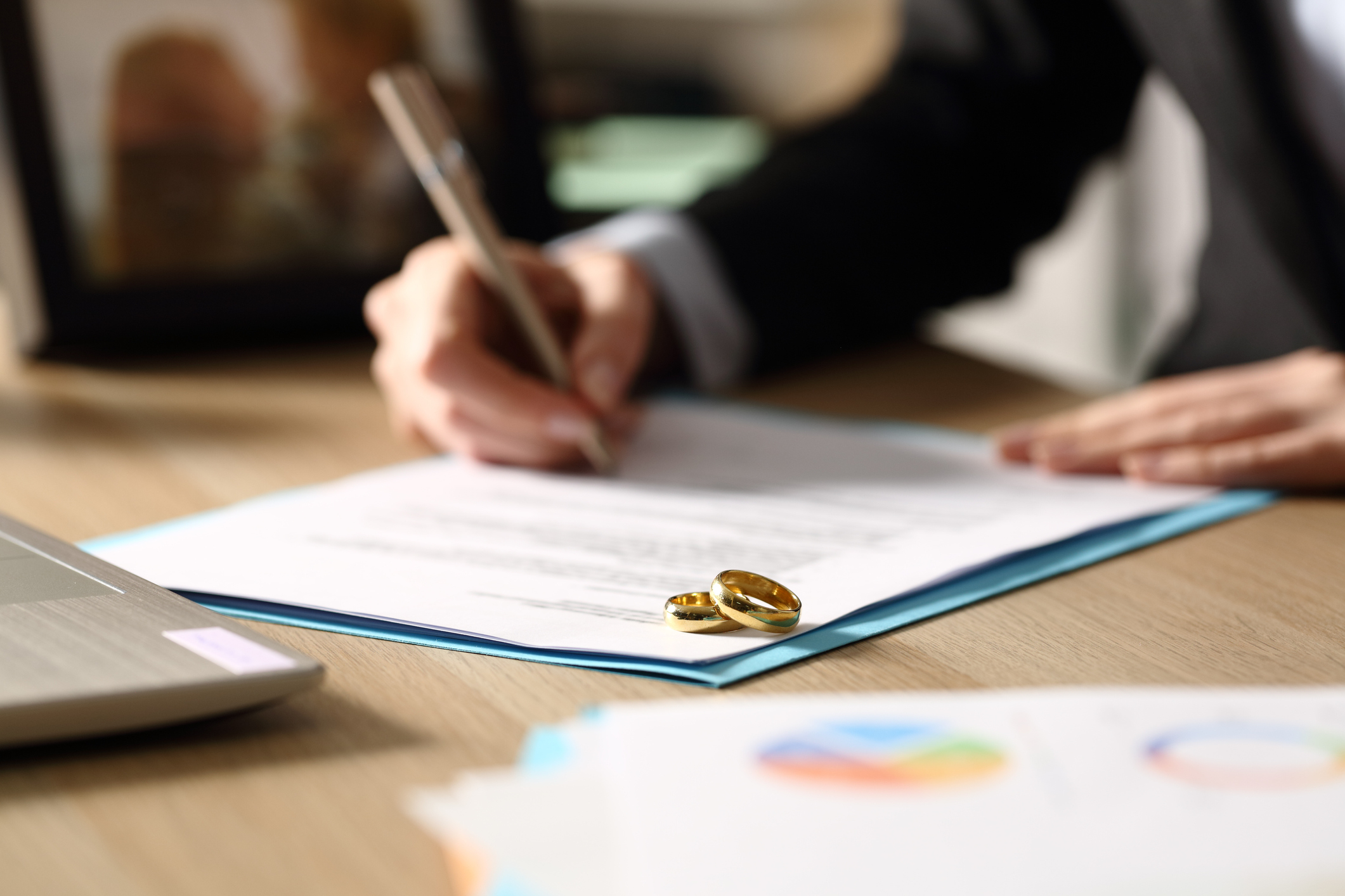 A person signing divorce papers with two wedding bands on the corner of the paper