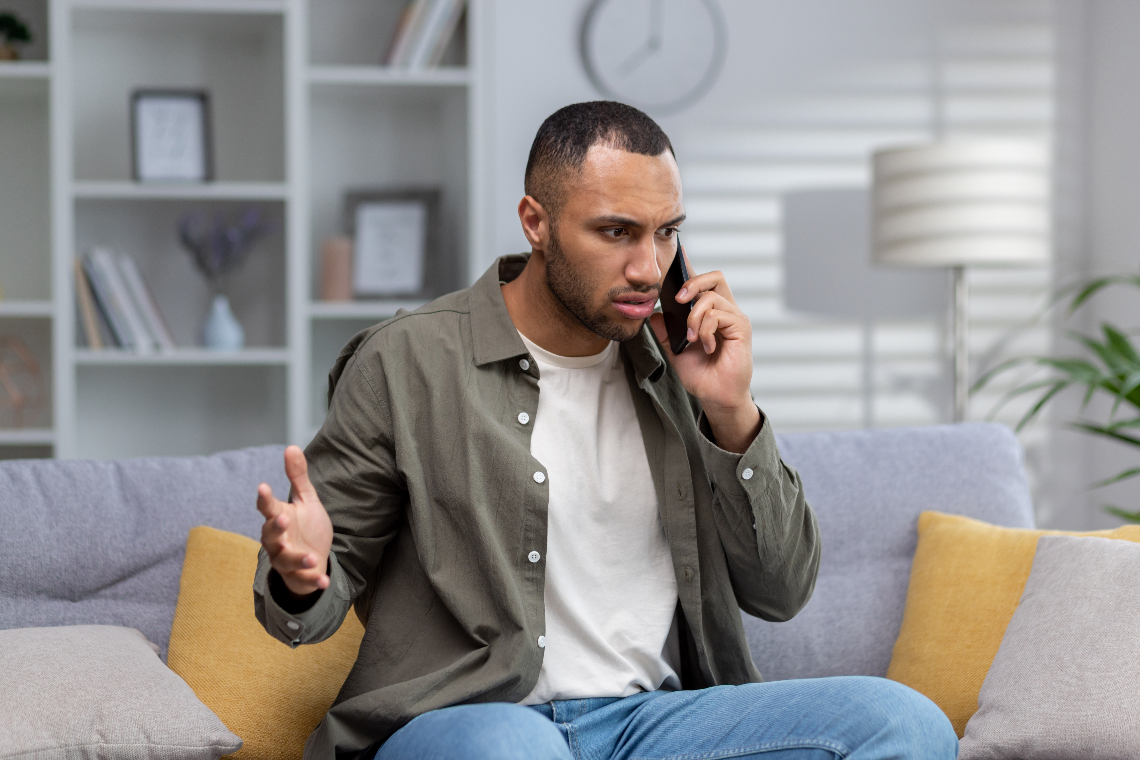 A man sitting on a couch and arguing with someone on the phone