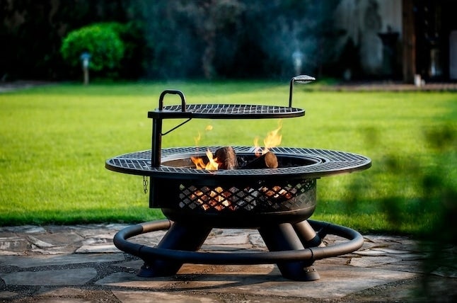 A wood burning fire pit with grill outside in a yard