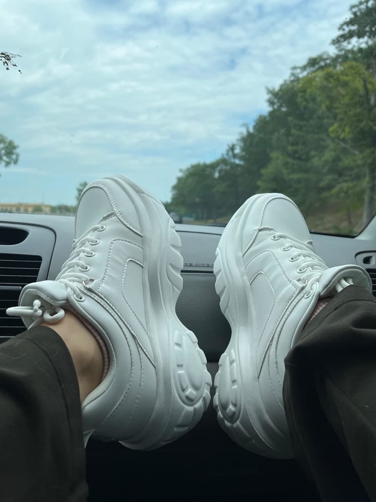 A reviewer in the all white sneakers with feet kicked up on a car dashboard