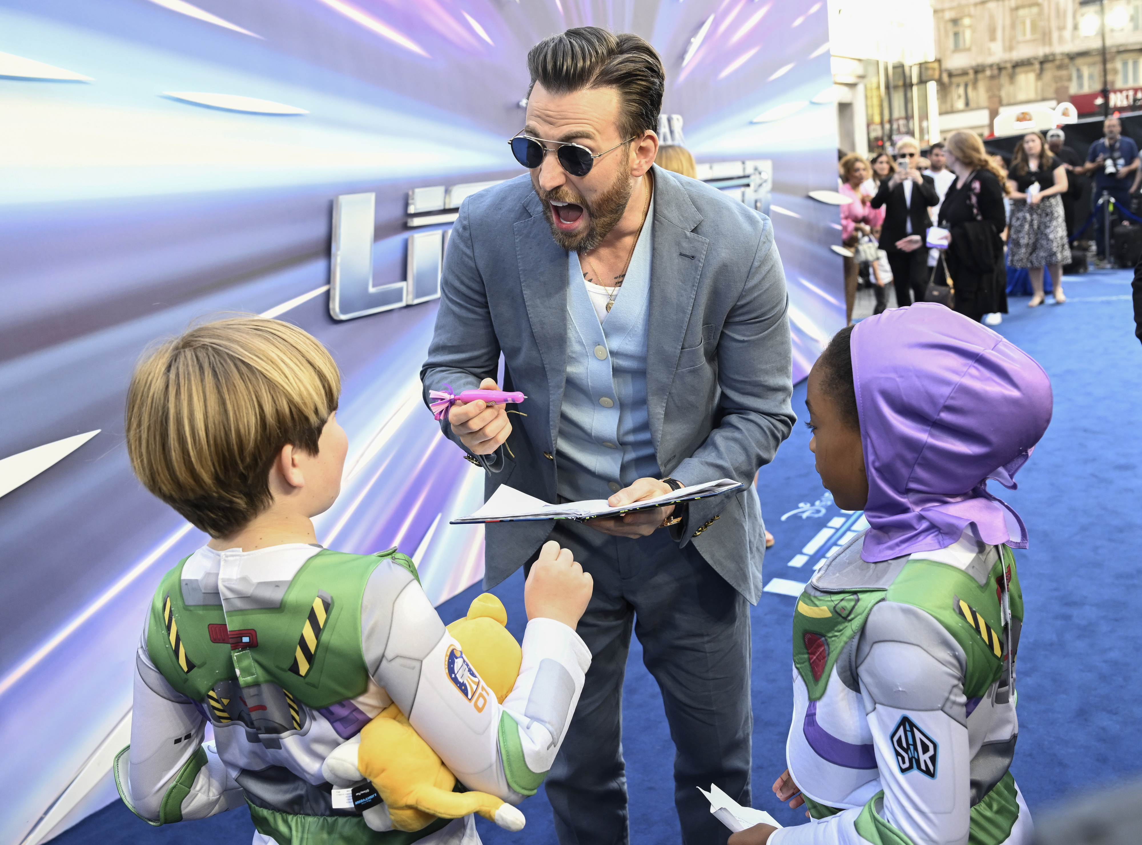 Chris Evans signing his autograph for two kids dressed like Buzz Lightyear at his movie premiere