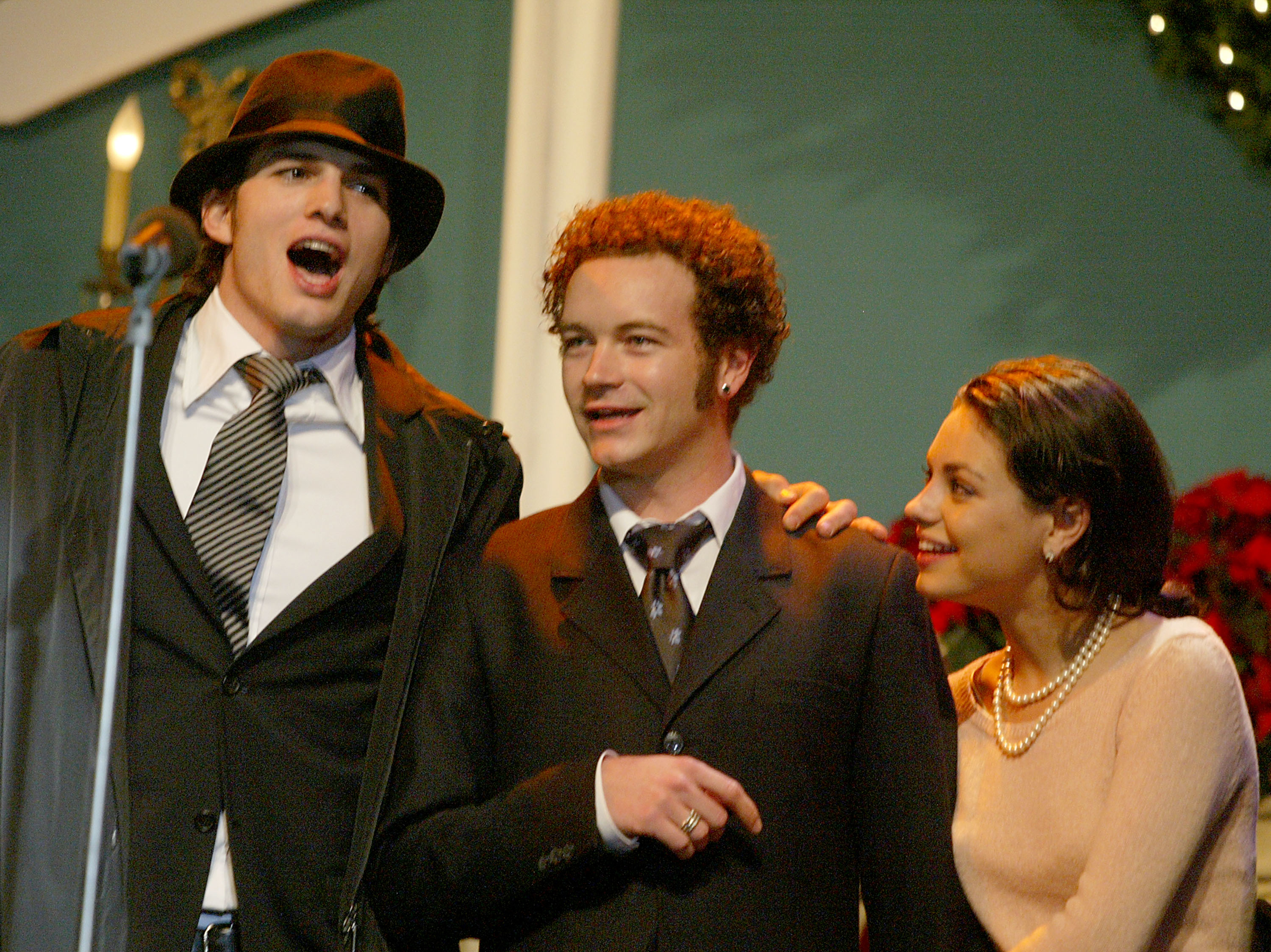 Close-up of Ashton , Danny, and Mila standing in front of a microphone