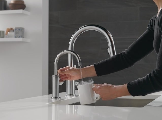 a person using the hot water tap to fill a mug