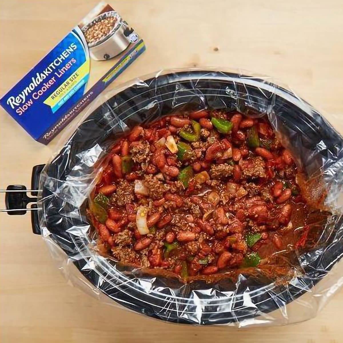 a reviewer photo of the box of liners with one inserted into a crockpot with food in it