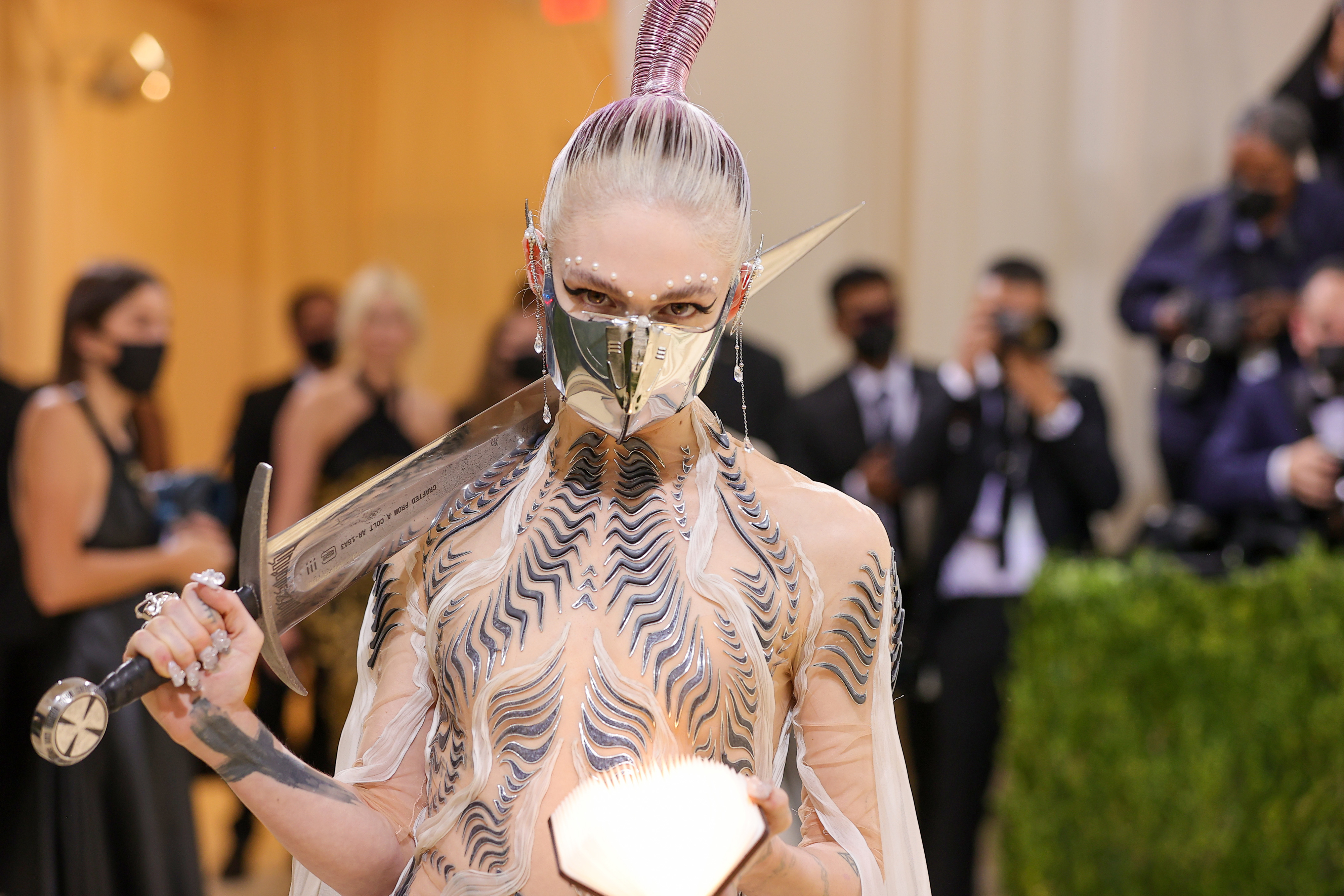 Grimes at a red carpet event in a ethereal Iras van Herpen dress and a metal face mask. Grimes os also carrying a sword