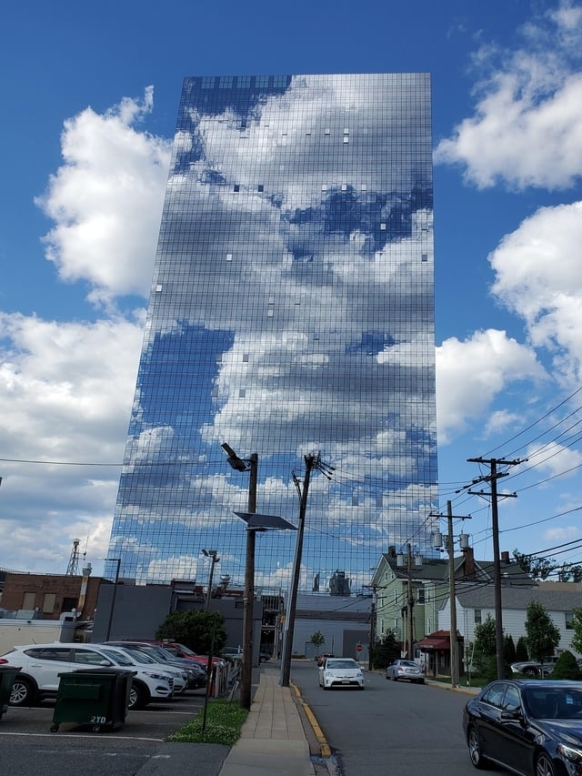 glass building has clouds reflected on it to blend with the sky